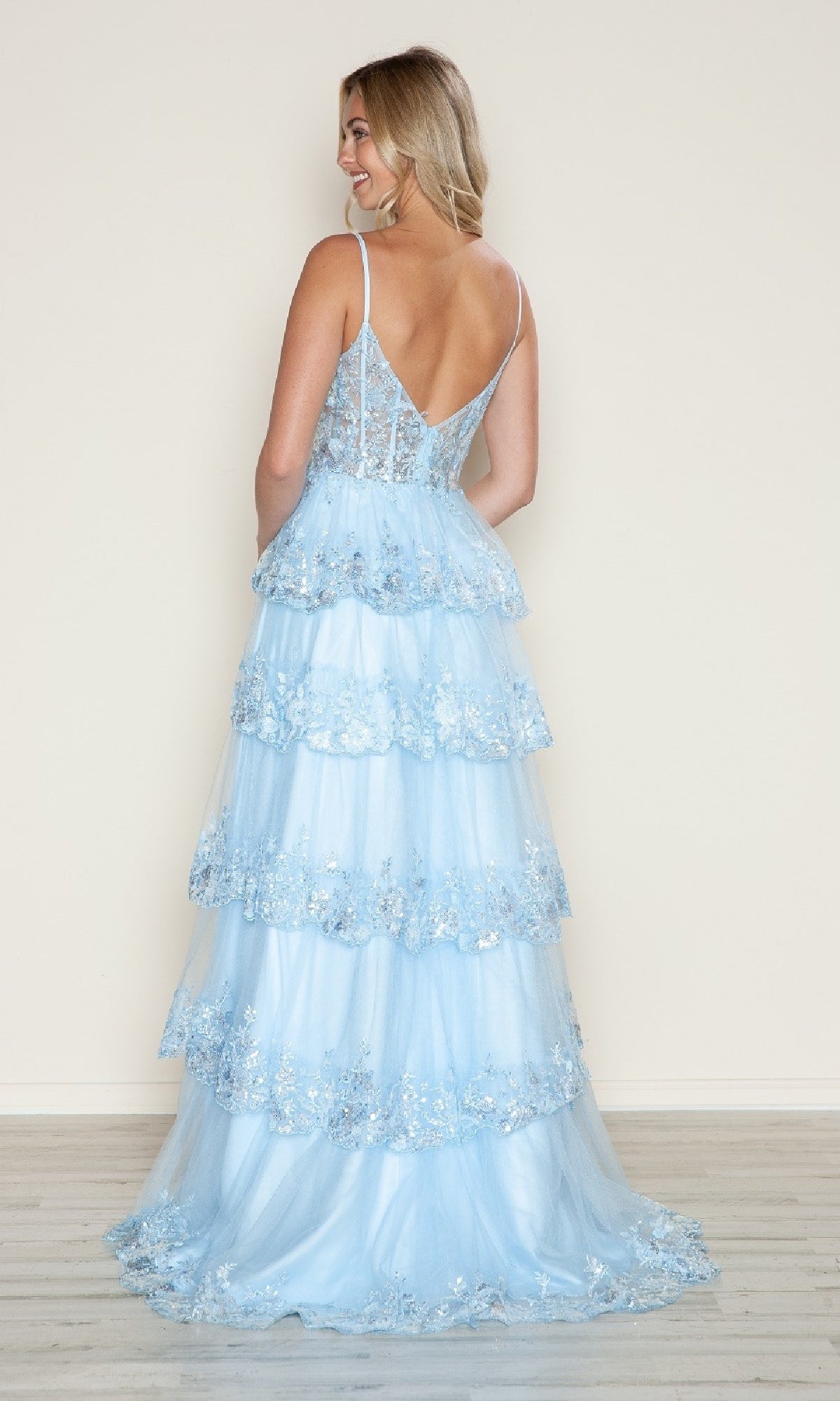 A woman in the Long Glitter-Lace Tiered Prom Dress (Poly USA 9548), a light blue, floor-length gown with floral glitter-lace and thin straps, stands with her back to the camera against a plain background.